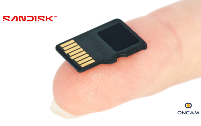 A close-up of a person's hand holding a SanDisk 2TB micro SD card between their thumb and forefinger, about to insert it into the side of a black electronic device.